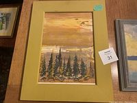 Framed painting of pine trees under warm sky in yellow frame with label showing lot number 31