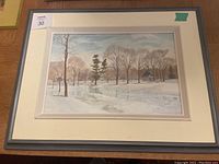 Front view of original oil painting depicting a winter landscape with trees and a cabin, framed and matted under glass.