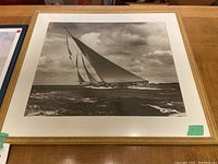 Black and white framed sailboat print showing a sailboat leaning into the wind on waves with cloudy sky.