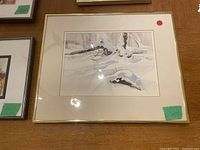 Framed watercolor painting of snow covered branches on a wooden surface