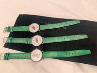 Three vintage Babar wristwatches laid flat showing green crocodile leather textured straps and different character faces.