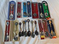 Full view of 17 vintage collector spoons arranged on white cloth, some in display boxes, some loose