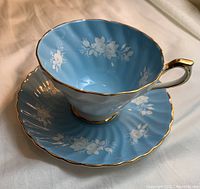 Close-up of the light blue tea cup with white floral pattern and gold trim highlight, placed on matching saucer.