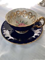 Dark blue Aynsley tea cup on matching saucer on white background showing side and handle with gold accents