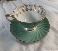 Side view of tea cup on saucer showing light green swirl pattern and gold detailing.