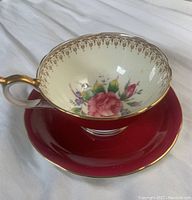 Tea cup with rose floral design and red saucer, showing design and gold trim details.