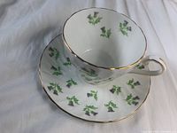 Photo of the teacup inside the matching saucer showing the green and purple thistle pattern with gold rims.
