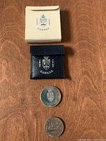 1976 silver dollar coin and 1967 Confederation coin displayed with original white outer box and blue inner case with shield emblem.