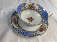 Tea cup displayed on top of matching saucer, showing floral design with blue and gold decorative banding.