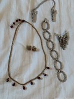 Full view of jewelry lot showing necklace with red rhinestone drops, link bracelet with clear rhinestones, raspberry-shaped clip-on earrings, and cascade rhinestone pin.