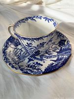 Blue and white Royal Crown Derby tea cup and matching saucer, showing the cup with a visible crack inside and gold trim edges.