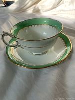 Tea cup and saucer shown together, highlighting shape and color combination of green, white and gold trim