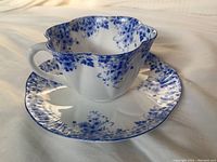 Close-up image of a Shelley fine bone china tea cup and saucer with blue floral pattern, showing scalloped edges and handle detail.