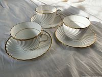 Three Aynsley bone china tea cups paired with saucers featuring a white swirl design and gold trim