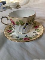 Tea cup and saucer set displayed to show floral design, scalloped edges, and gold trim.