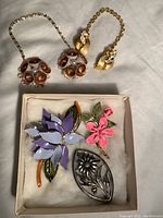 Overall view of vintage brooches and sweater clips showing floral enamel brooches and gold-tone clips with rhinestones.