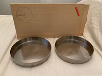 Two round vintage stainless steel serving bowls from Cylinda-Line by Arne Jacobsen, positioned side by side in front of original box.