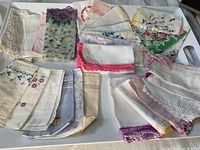 Top-down photo showing the collection of vintage handkerchiefs and doilies arranged on a white tray with a measurement tool for scale, showing various floral patterns and colors.