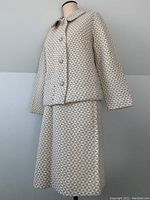 Full suit displayed on mannequin featuring jacket and skirt with geometric pattern in cream and silver metallic design.