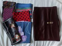 Five assorted scarves folded and arranged on a white surface next to a vintage dark brown leather briefcase