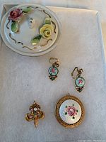 Porcelain container with lid and four jewelry pieces arranged inside, showing the complete lot