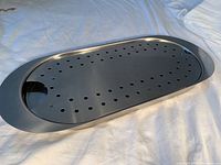 Overall view of the stainless steel steaming tray with perforated black insert placed on a white cloth background.