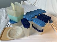 Various sizes of vintage translucent plastic Tupperware containers with blue flip-top lids, some stacked, displayed on a white surface