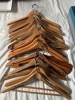 Top view of 15 wooden clothes hangers with metal hooks stacked together showing the text markings on the wood sides.