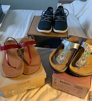 Photo showing all three pairs of shoes with their original boxes. Black sneakers placed on one box, metallic sandals on another, red Coach sandals on another box.