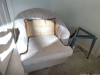 Off-white swivel armchair, beige carpet, gold throw pillow, triangular glass top side table adjacent to chair.