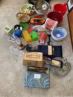 Photo showing assortment of colorful canisters, mixing bowls, wicker basket, cheese spreader, and boxed kits alongside kitchen tools and dish towels.