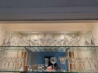 Large assortment of stemware displayed on mirrored glass shelves including margarita, martini, and wine glasses with colorful swirl and stripe patterns plus several shot glasses on bottom shelf.
