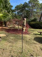 Bird feeder hanging on a black metal stand set in a grassy yard.