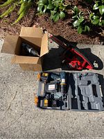 Wider view showing all items together: Homelite chainsaw, Ryobi cordless drill set in molded case and additional drill in box.