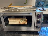 Front view of stainless steel Cuisinart convection toaster oven broiler with knobs and accessories on top