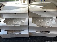 Stack of six white boxes containing multiple sets of DANSK champagne flutes visible through box openings