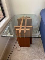 Glass top side table with wooden base, photographed from the side showing the thickness and clear finish of the glass and the structure of the wooden base.