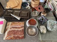 Overview of the mixed lot on a gray surface, shows various kitchen and decorative items including marble cutting board, pottery, pewter items, and more.