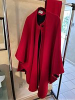 Front view of the red wool and cashmere coat cape hanging on a rack, showing the loose draping and one-button closure.