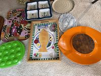 Full view of eight assorted serving platters and trays laid on carpeted floor, including colorful, ceramic, plastic, and marble materials.