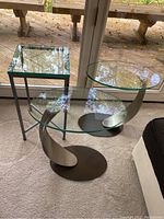 Three side tables grouped together on carpet: two with round glass tops and twisted metal bases, one with square glass top and simple metal frame.