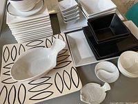 Top down view of white square plates, small bowls, black square bowls, and a large platter with black leaf pattern.