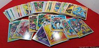 Photo showing a box lot of colorful trading cards from 1991 Impel Marvel Series 2, laid out overlapping on a red surface, featuring characters like Spider-Man, Captain America, Iron Man, Thor, and others.