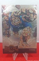 Front of the trading card showing The Thing character with metallic foil background.