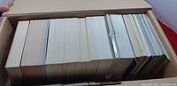 Top view of a cardboard box filled with a large quantity of mixed trading cards with some in sleeves