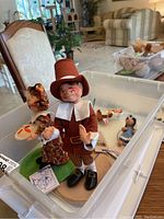 Two Annalee Thanksgiving Pilgrim dolls, man and woman, inside a plastic bin with tags visible.