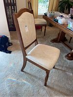 Single wooden dining chair with light beige upholstered seat and backrest, carved wooden top, turned front legs, showing need for cleaning.