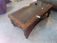 Full view of coffee table showing glass top, carved wooden frame, and light tile floor background.