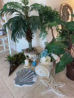 Overview showing multiple faux plants, beach decor pieces, candle, and coral stopper bottle