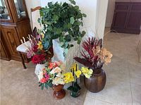 Image showing five faux plants arranged in various vases around a white textured pedestal on tiled floor.